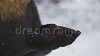 在一场降雪中，一个女人把戴着手套的手举在她面前，享受着降雪。